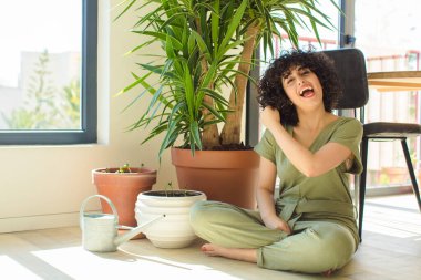 Genç, güzel bir Arap kadın evinde, elinde bir su bidonu ve bitkilerle.