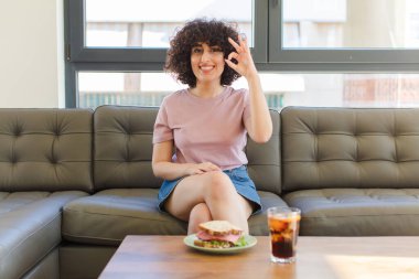 Genç, güzel bir Arap kadın evdeki kanepede sandviç yiyor.