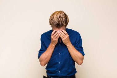 Sarışın, beyaz bir adam üzgün, hayal kırıklığına uğramış, gergin ve depresif, iki eliyle yüzünü kaplayan, ağlayan.