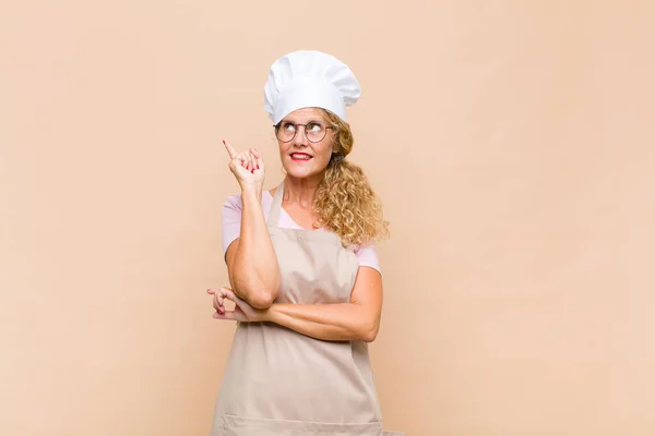 middle age woman baker smiling happily and looking sideways, wondering, thinking or having an idea