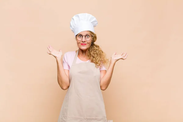 中年の女性のパン屋は困惑し混乱し または面白い表現で異なるオプションを選択します — ストック写真