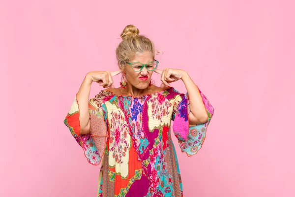 Orta yaşlı bir kadın sinirli, stresli ve sinirli görünüyor, iki kulağını da sağır edici bir ses, ses ya da yüksek sesle kapatıyor.