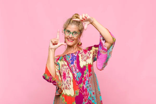 Orta yaşlı bir kadın mutlu, arkadaş canlısı ve pozitif hissediyor, gülümsüyor ve elleriyle bir portre veya fotoğraf çerçevesi yapıyor.