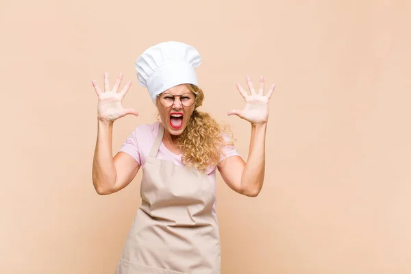 中年の女性のパン屋はパニックや怒りで叫んでショックを受け恐怖や激怒し頭の横に手を置いて — ストック写真
