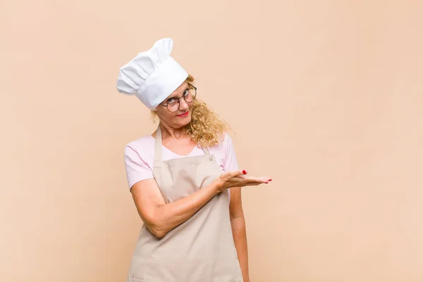 middle age woman baker smiling cheerfully, feeling happy and showing a concept in copy space with palm of hand