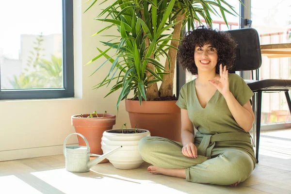 Genç, güzel bir Arap kadın evinde, elinde bir su bidonu ve bitkilerle.