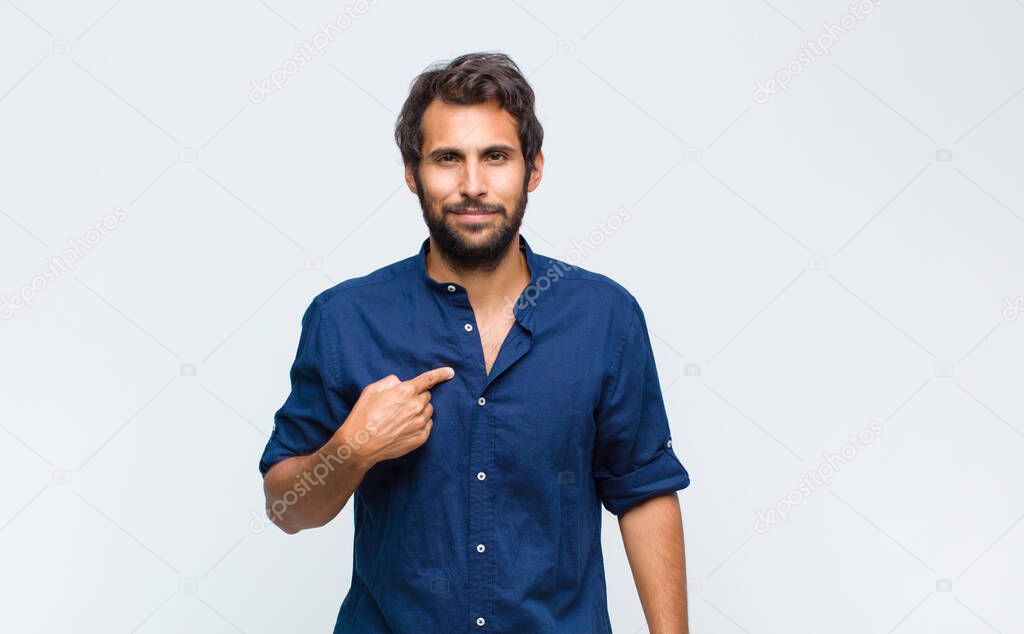 young latin handsome man looking proud, confident and happy, smiling and pointing to self or making number one sign