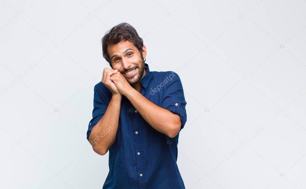 young latin handsome man feeling in love and looking cute, adorable and happy, smiling romantically with hands next to face
