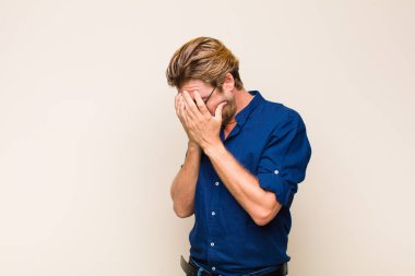 Sarışın, beyaz bir adam üzgün, hayal kırıklığına uğramış bir bakışla gözlerini kapatıyor. Ağlıyor, yan gözle bakıyor.