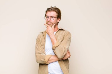 Sarışın, beyaz bir adam ciddi, düşünceli ve güvensiz görünüyor. Bir kolu çapraz, eli çenesinde, seçenekleri tartıyor.