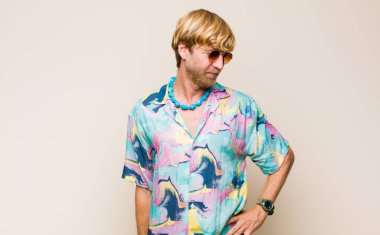 Sarışın, beyaz bir adam mutlu bir şekilde gülümsüyor, eli kalçasında ve kendinden emin, olumlu, gururlu ve arkadaş canlısı.