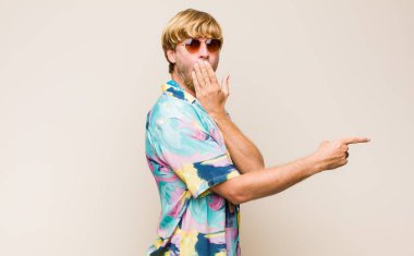 Sarışın, beyaz bir adam mutlu, şok olmuş ve şaşırmış hissediyor. Ağzını eliyle kapatıyor ve yanal fotokopi alanını işaret ediyor.