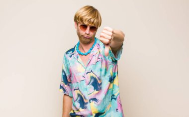 Sarışın, beyaz bir adam kızgın, sinirli, hayal kırıklığına uğramış ya da hoşnutsuz, ciddi bir bakışla başparmağını kaldırıyor.