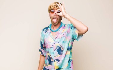 Sarışın, beyaz bir adam komik yüzüyle mutlu bir şekilde gülümsüyor, şaka yapıyor ve gözetleme deliğinden bakıyor, sırları gözetliyor.