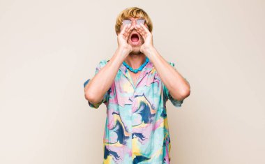 Sarışın, beyaz bir adam mutlu, heyecanlı ve pozitif hissediyor. Elleri ağızda, bağırıyor.