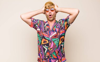 Sarışın, yetişkin bir gezgin heyecanlı ve şaşırmış görünüyor, ağzı açık, iki eli başında, kendini şanslı bir kazanan gibi hissediyor.