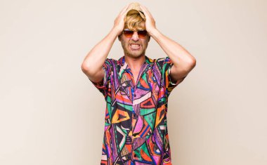 Sarışın, yetişkin, gergin, bunalımlı ve hayal kırıklığına uğramış, iki elini de başa kaldıran bir gezgin.