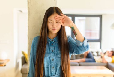 Genç ve güzel Asyalı kadın stresli görünüyor, yorgun ve hayal kırıklığına uğramış, alnından ter damlıyor, umutsuz ve bitkin hissediyor.