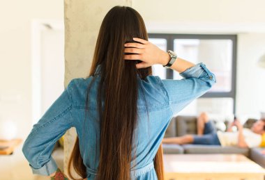 Genç, güzel Asyalı kadın düşünüyor ya da şüphe ediyor, kafasını kaşıyor, kafası karışık ve kafası karışık, arkaya ya da arkaya bakıyor.