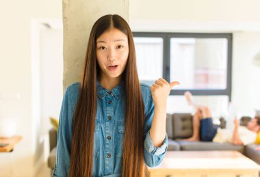 Genç ve güzel Asyalı bir kadın inançsızlıktan şaşkın şaşkın bakıyor, yan taraftaki objeyi işaret ediyor ve 