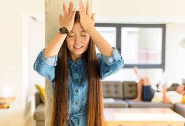 Genç ve güzel Asyalı kadın stresli ve endişeli hissediyor, bunalımda ve hayal kırıklığına uğramış, iki elini de başa kaldırıyor.