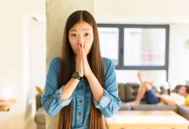 Genç, güzel Asyalı kadın endişeli, üzgün ve korkmuş hissediyor. Ağzını ellerle kapatıyor. Endişeli ve berbat görünüyor.