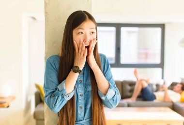 Genç, güzel Asyalı kadın mutlu, heyecanlı ve şaşırmış hissediyor. İki eli yüzü de havada bir tarafa bakıyor.