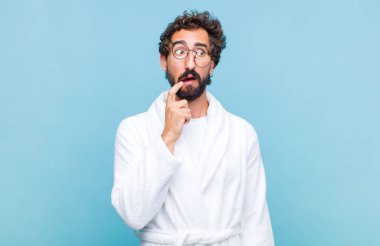 Banyo cübbesi giyen genç sakallı bir adam şaşırmış, gergin, endişeli ya da korkmuş bakışları ile, fotokopi alanına doğru yan bakıyor.