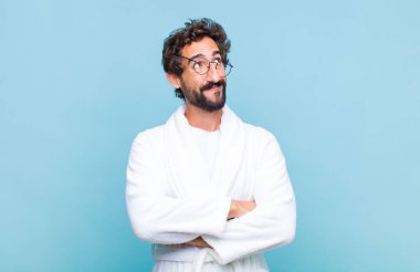 Banyo bornozu giyen genç sakallı adam mutlu, gururlu ve umutlu hissediyor, merak ediyor ya da düşünüyor, çapraz kollarıyla kopya alanı arıyor.