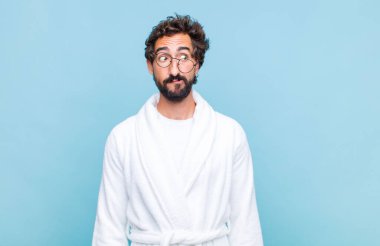 Banyo cübbesi giyen genç sakallı adam endişeli, stresli, endişeli ve korkmuş görünüyor, panikliyor ve dişlerini sıkıyor.