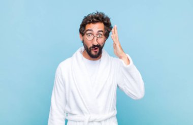 Banyo bornozu giyen genç sakallı adam mutlu, şaşkın ve şaşırmış görünüyor, gülümsüyor ve inanılmaz ve inanılmaz iyi haberleri fark ediyor.