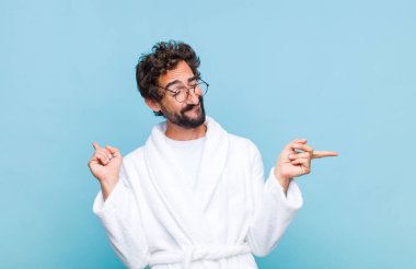 Genç sakallı adam banyo cübbesi giyiyor gülümsüyor, tasasız ve mutlu hissediyor, dans ediyor ve müzik dinliyor, bir partide eğleniyor.