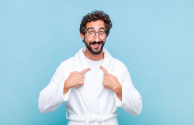 Banyo bornozu giyen genç sakallı adam mutlu, şaşkın ve gururlu hissediyordu. Heyecanlı ve şaşkın bir bakışla kendini gösteriyordu.