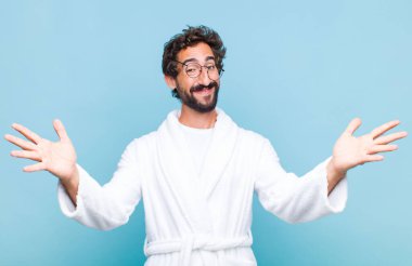 Banyo bornozu giymiş genç sakallı adam neşeyle gülümsüyor sıcak, dostça, sevgi dolu bir kucak veriyor, mutlu ve sevimli hissediyor.