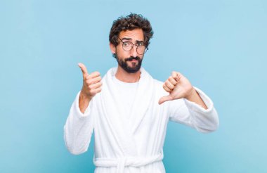 Banyo bornozu giyen genç sakallı adam kafası karışık, bilgisiz ve emin olmayan farklı seçeneklerle iyiyi ve kötüyü tartıyor.