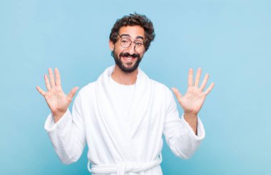 Banyo bornozu giymiş genç sakallı adam gülümsüyor ve arkadaş canlısı görünüyor, onuncu ya da onuncu numarayı gösteriyor, eli önde, geri sayıyor.