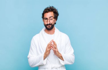 Genç sakallı bir adam banyolu bornoz giyer gururlu, haylaz ve kibirli bir şekilde şeytanca bir plan kurar ya da bir numara düşünür.