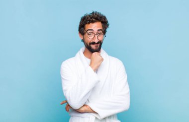 Genç sakallı adam banyo cübbesi giyiyor gülümsüyor, hayattan zevk alıyor, mutlu, arkadaş canlısı, tatmin olmuş ve tasasız.