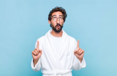 Banyo bornozu giyen genç sakallı adam şaşırmış, şaşırmış ve ağzı açık bir şekilde iki elini de havaya kaldırıp uzayı kopyalamaya çalışıyor.