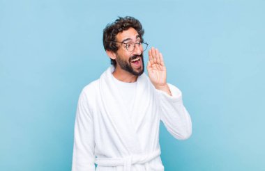 Banyo cübbesi giyen genç sakallı adam, mutlu ve heyecanlı görünüyor, bağırıyor ve bir yandan da fotokopi çekmek için arıyor.