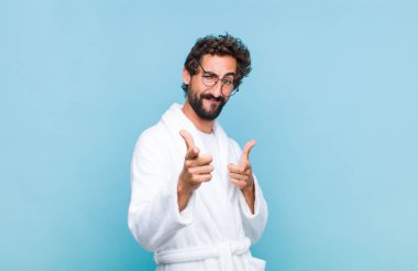 Banyo bornozu giyen genç sakallı adam kendini mutlu, sakin, rahat ve başarılı hissediyor. Kameraya bakıyor ve seni seçiyor.