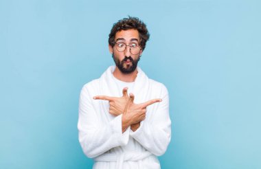 Banyo bornozu giymiş genç sakallı adam şaşkın ve şaşkın görünüyor, güvensiz ve zıt yönlere şüpheyle bakıyor.