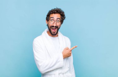 Banyo bornozu giymiş genç sakallı adam heyecanlı ve şaşırmış görünüyor.