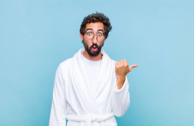 Banyo bornozu giymiş genç sakallı adam inançsızlıktan şaşkın şaşkın bakıyor, yan taraftaki objeyi işaret ediyor ve diyor ki: