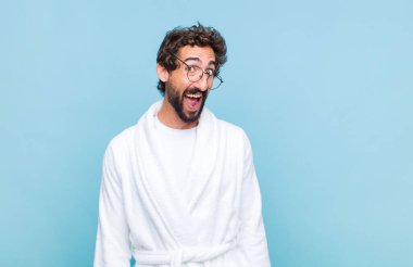 Genç sakallı bir adam banyo cübbesi giyiyor. Büyük, dostane, kaygısız bir gülümsemesi var. Olumlu, rahat ve mutlu görünüyor.