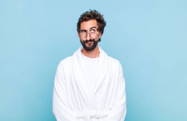 Banyo bornozu giymiş genç sakallı bir adam kafası karışmış ve kafası karışmış görünüyor. Bir sorunu çözmeye çalışıyor ya da çözmeye çalışıyor.