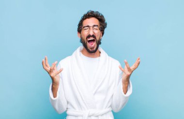 Banyo bornozu giymiş genç sakallı adam öfkeyle bağırıyor, stresli hissediyor ve ellerini havaya kaldırıp neden benim...