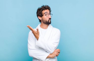 Banyo bornozu giyen genç sakallı adam kafası karışık ve habersiz, şüpheli bir açıklama ya da düşünce hakkında merak ediyor.