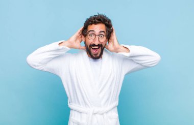 Banyo bornozu giyen genç sakallı adam mutlu, kaygısız, arkadaş canlısı ve rahat görünüyor. Hayattan ve başarıdan keyif alıyor, olumlu bir tavırla.