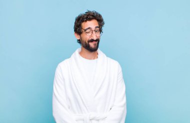 Genç sakallı adam banyo cübbesi giyiyor. Mutlu ve arkadaş canlısı görünüyor. Gülümsüyor ve sana olumlu bir tavırla göz kırpıyor.